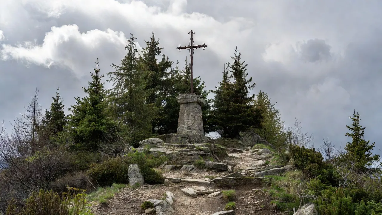 Calvaire de pierre au sommet d'un sentier de montagne en Savoie, croix ancienne entourée de sapins